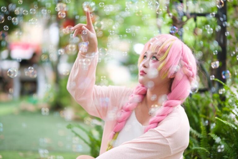 A young woman with pink hair surrounded by bubbles in a lush garden.